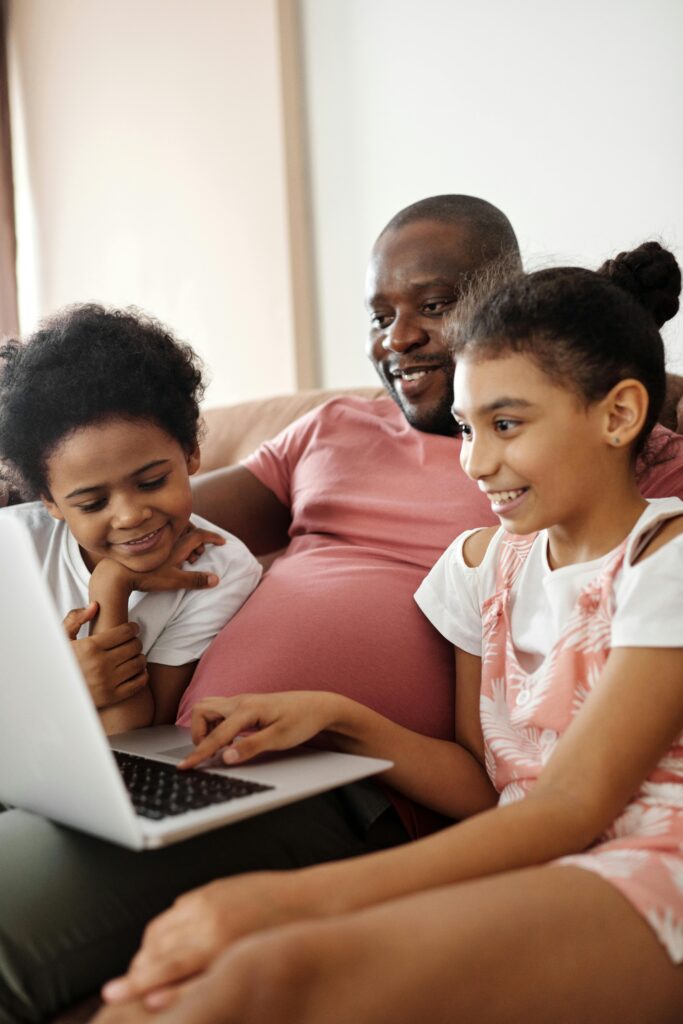 Smiling father and kids using a laptop at home, sharing joyful moments.