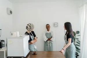 pexels-photo-4349915-4349915 Three female baristas chatting and smiling in a modern, bright cafe setting.